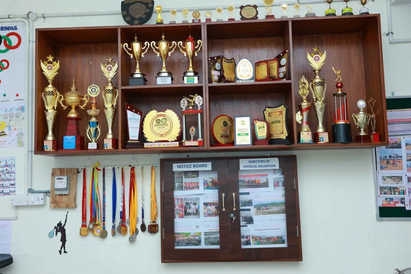 A cabinet of sports trophies and hanging medals above the physical education notice board.