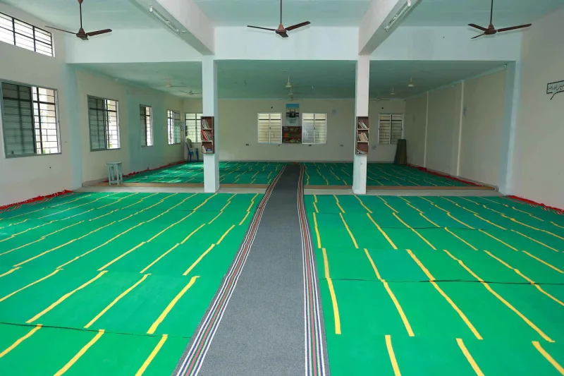 The prayer hall: a wide open hall laid with green prayer mats and a carpeted central walkway.