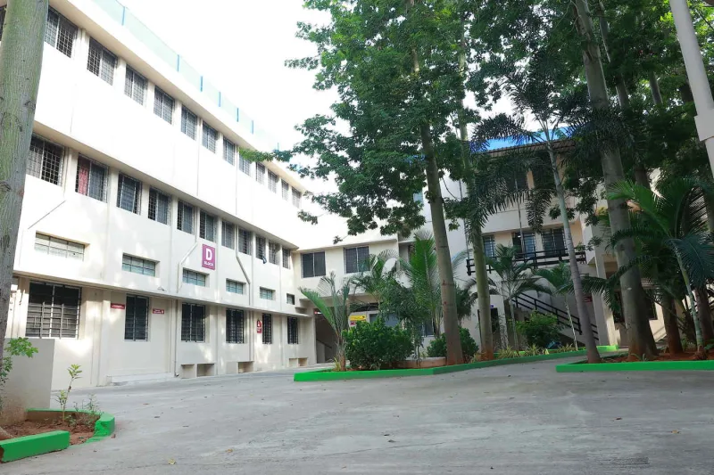 D Block seen from the courtyard, three storeys of classrooms behind palm trees.